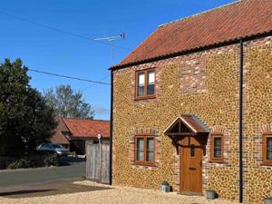 The brown cobbled exterior of 1a Stones Throw in Snettisham, West Norfolk. There are three front windows and one front door. The self-catering propert