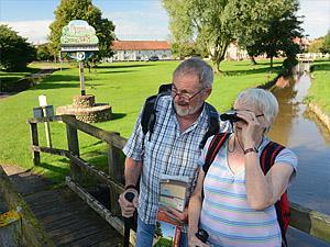A couple walking through South Creake in west Norfolk holding binoculars and maps.