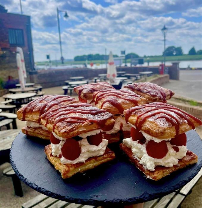 Image of cream cakes on a platter with a backdrop view of King's Lynn harbour